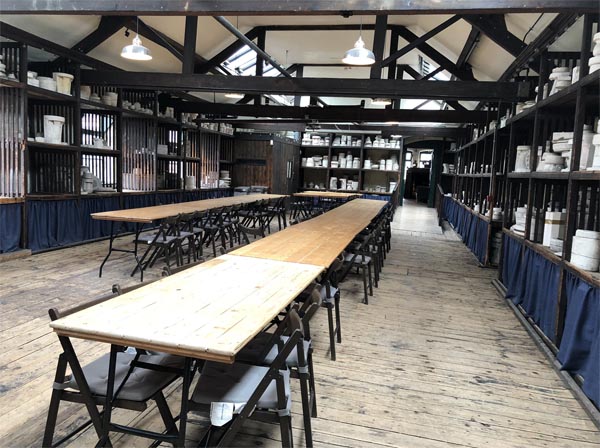 Room with long tables in centre, and chairs, where women once worked to paint pottery. Old pottery moulds are used to display shelves around the room 