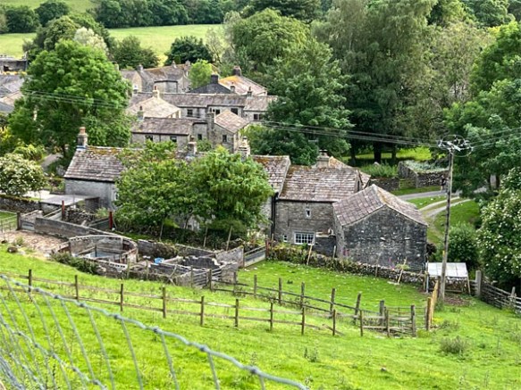 A rural village scene with seventeenth century stone houses surrounded by hills and trees